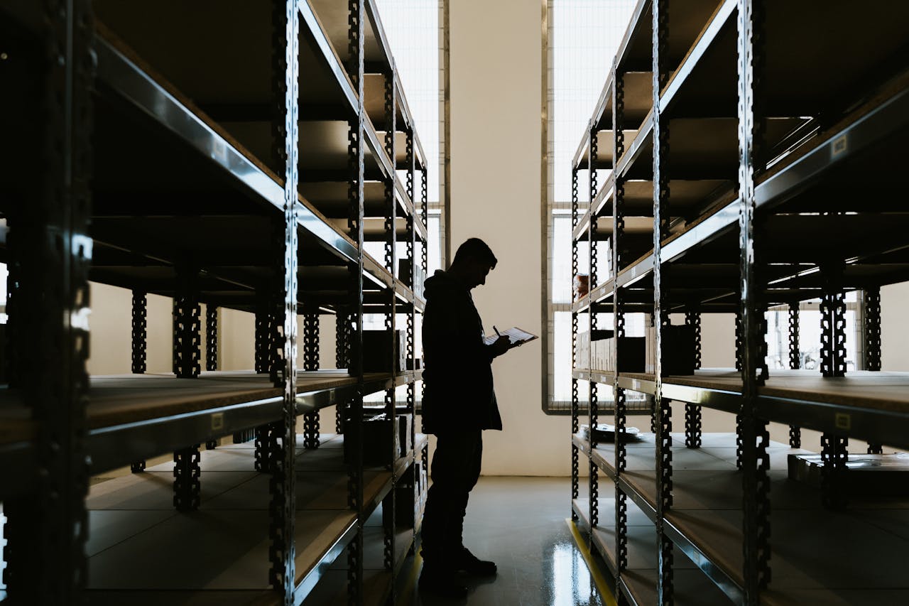 Silhouette of a person checking inventory in an empty warehouse with racks.